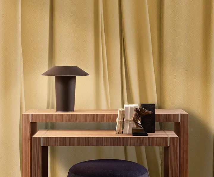 Una consolle di legno con una lampada davanti a una parete giallo oro dalle pieghe di tessuto